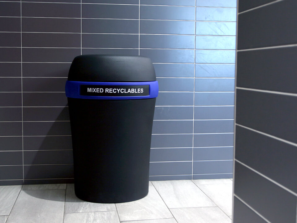 durable black plastic mixed recyclables container with a blue color band and large capacity body at the entrance to a shopping mall washroom area