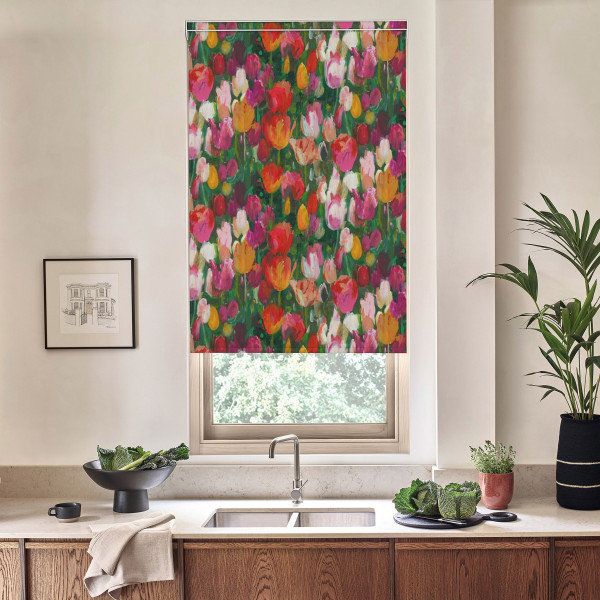 Floral roller blind covers window, displaying dense multicolored tulip pattern; kitchen sink and faucet sit below on marble countertop with bowls of greens, potted plants, and framed sketch on wall.