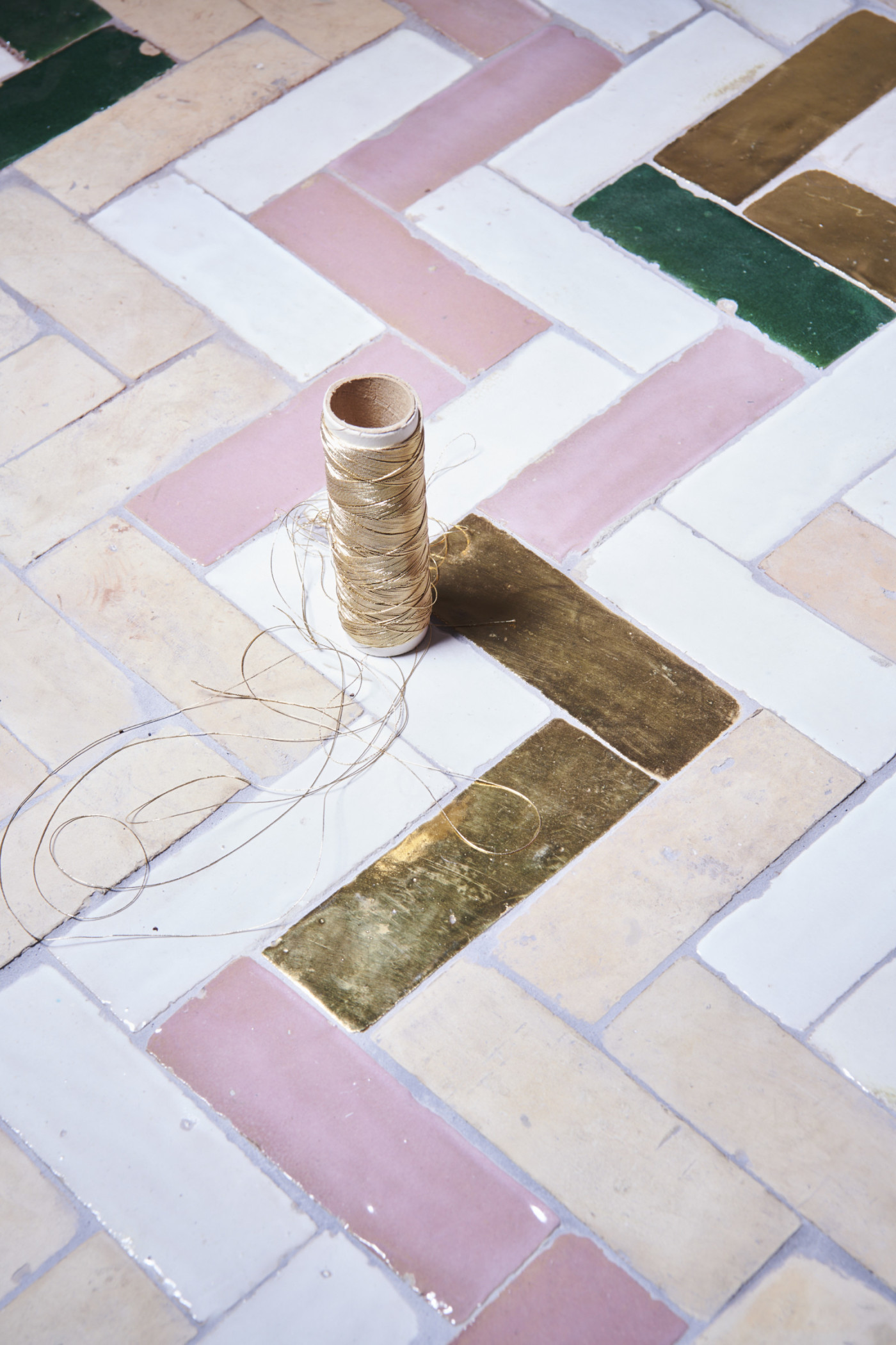 a pink and gold tiled floor with a spool of thread.