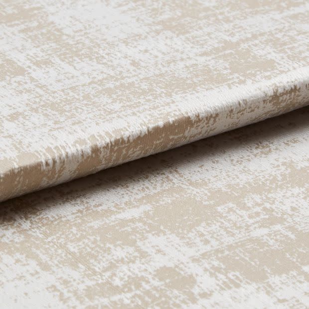 Beige-and-white distressed-pattern fabric panel with a horizontal fold, resembling a Roman blind; photographed close-up on a neutral surface under soft, even lighting.