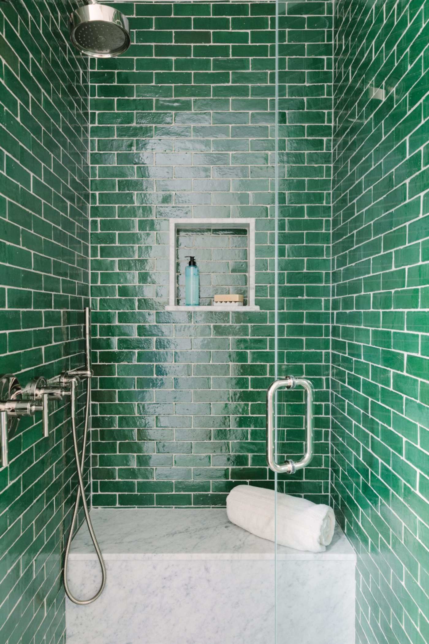 a green tiled shower with a glass shower door.