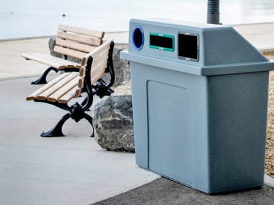 triple stream recycling and trash bin with a heavy duty LDPE plastic body and lid and color-coded restrictive openings outdoors at a local waterfront park