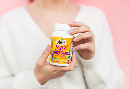 Woman in white sweater holding bottle of Alive Multivitamins Max3 Women's tablets.