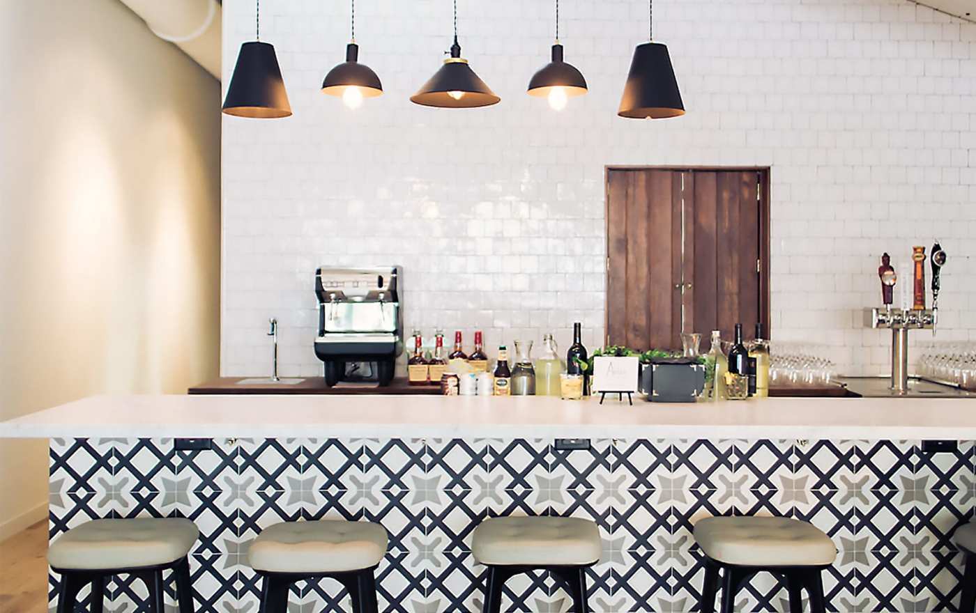 a bar with black and white tiled walls and stools.