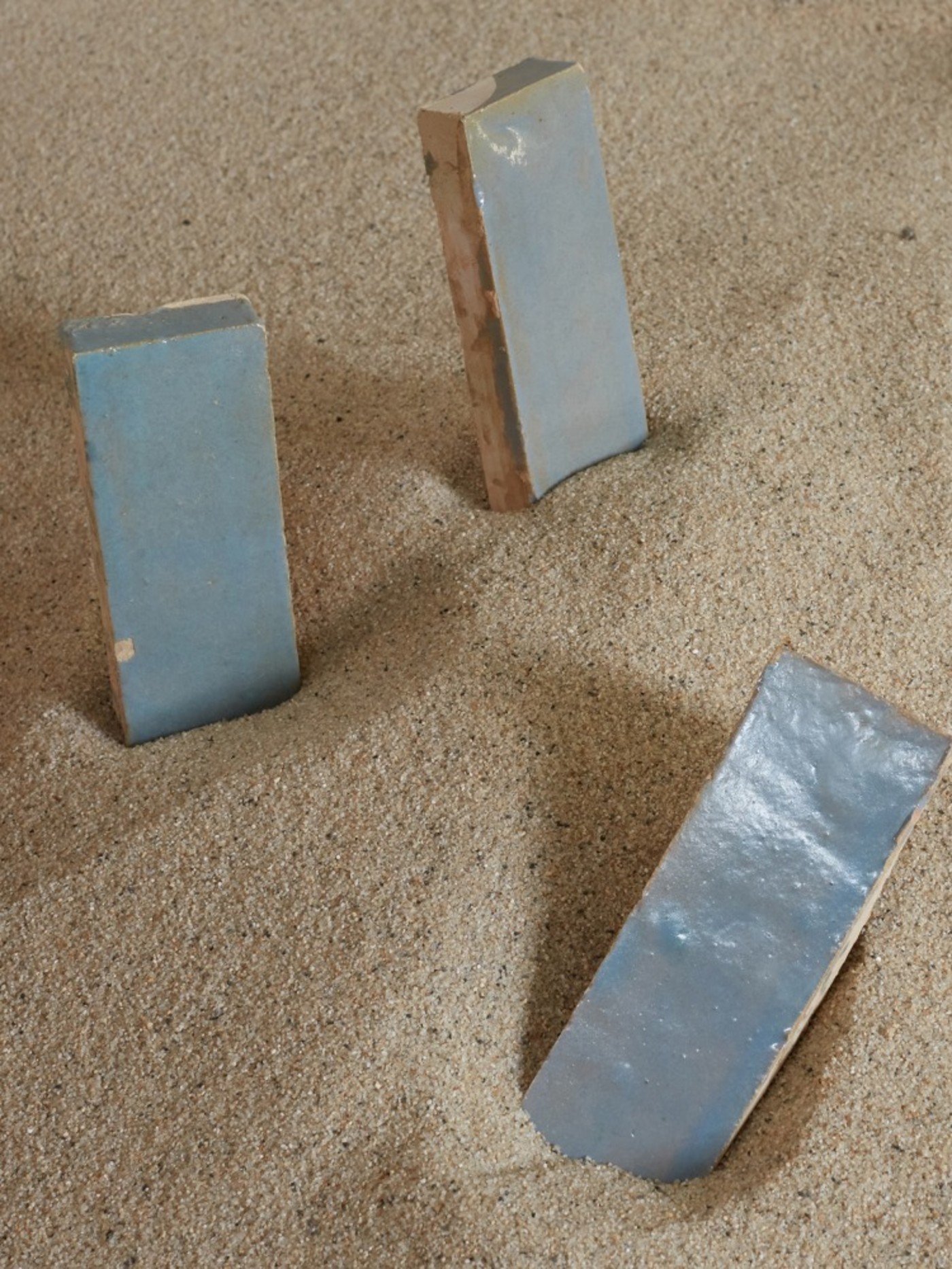 three blue tiles in the sand next to each other.