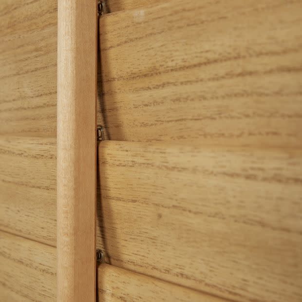 Wooden plantation shutters with a central vertical tilt rod and overlapping horizontal slats — closed, aligned to block light — close-up interior view showing warm wood grain and soft ambient light.