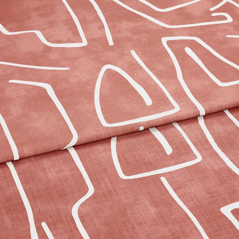 Folded patterned fabric: a roseâ€‘terracotta curtain-like textile with white abstract line motifs, folded once across the frame. Close-up studio view emphasizing soft woven texture and matte finish.