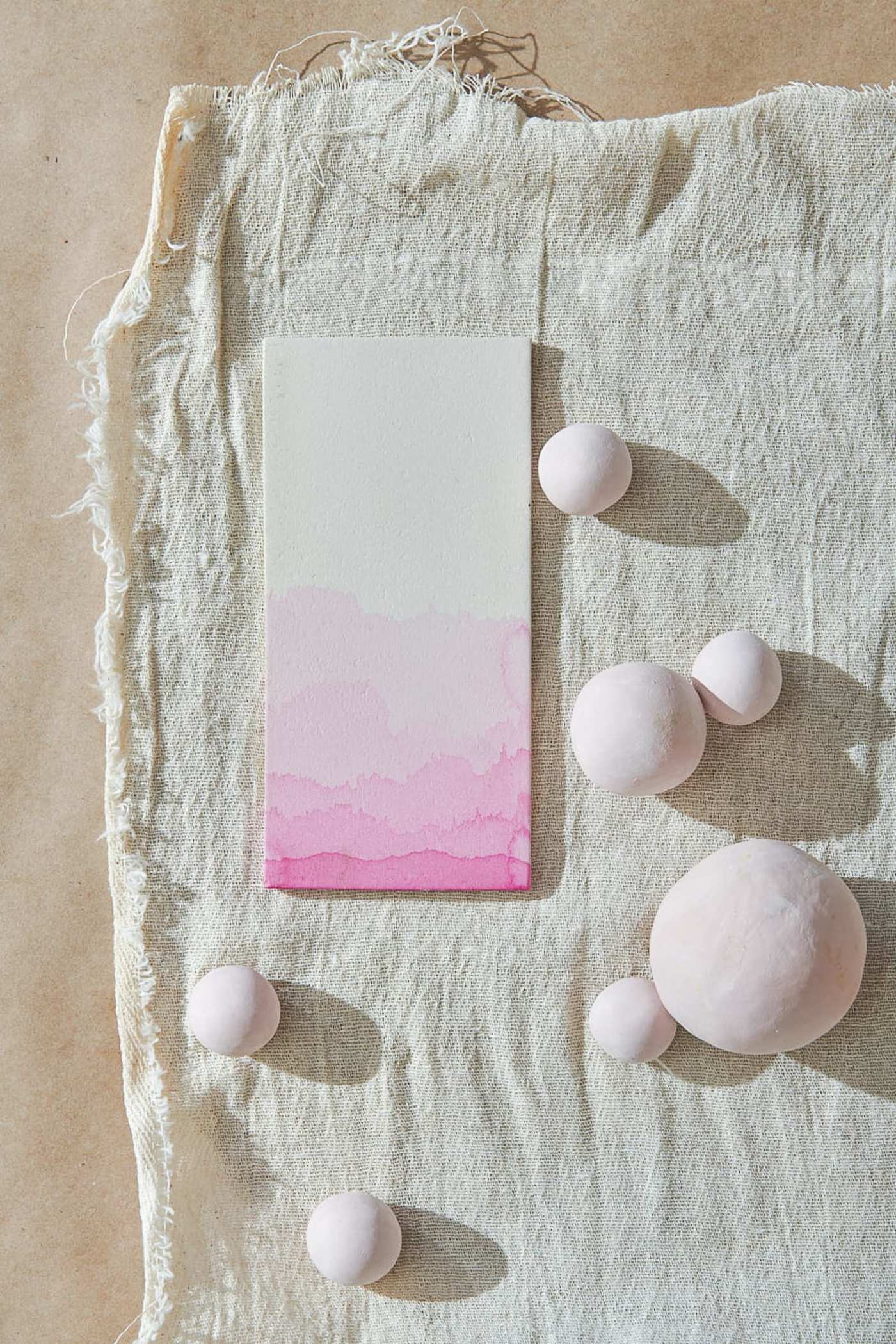 a pink and white patterned tile and round ceramic pieces on a piece of cloth.