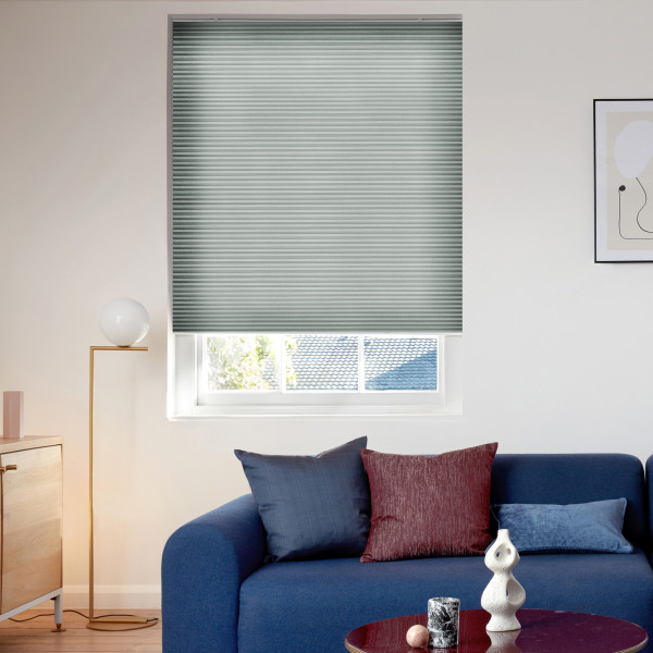 Pleated cellular blind, lowered almost fully with a narrow gap at the bottom and fine horizontal ribs, blocking and softly filtering daylight over a living room with blue sofa, lamp, and artwork.
