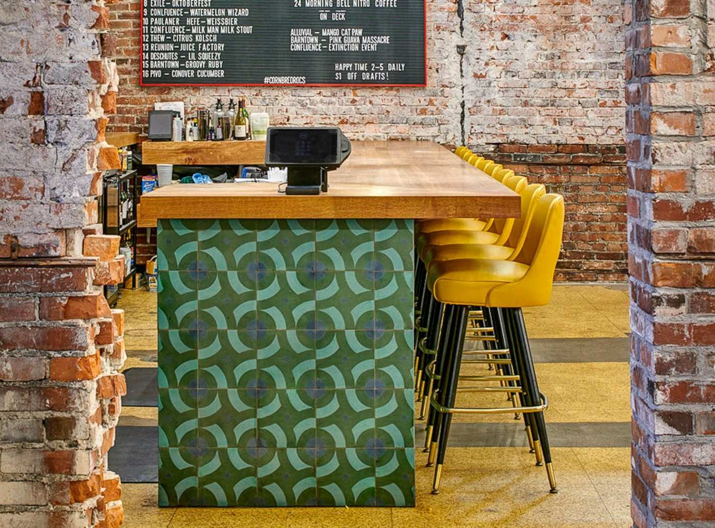 a bar with yellow stools, brick walls, and a green tiled counter.