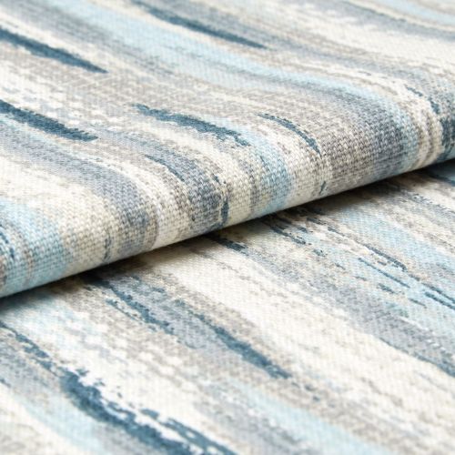 Low-pile woven rug with blue, gray, and cream abstract streaks; folded over itself; tight close-up studio view emphasizing woven texture and layered edges.