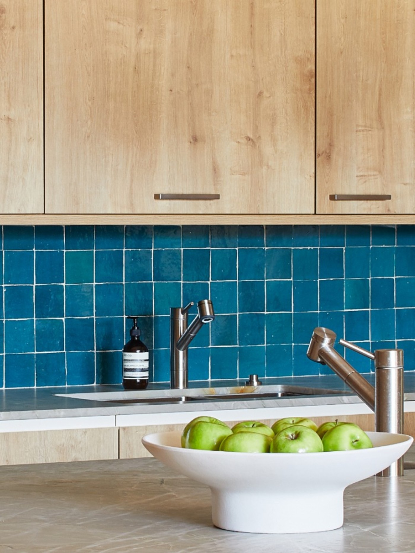 a blue tiled kitchen backsplash with a bowl of apples on a countertop.