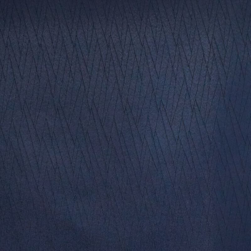 Navy-blue quilted fabric panel with narrow diagonal stitched diamonds, the quilting forming overlapping chevrons; close-up, evenly lit flat surface suggesting upholstery or textured wall covering.