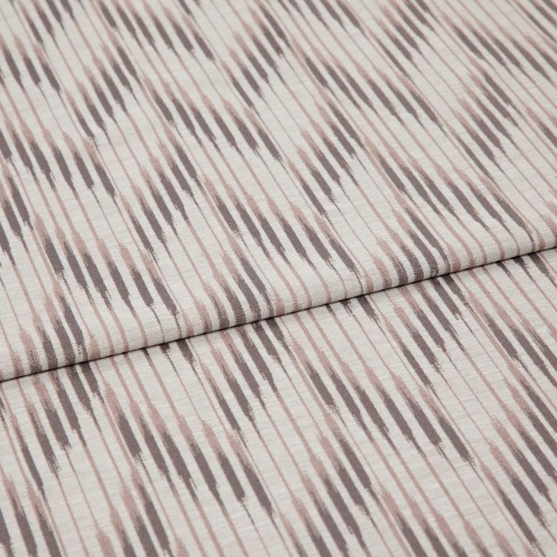 Folded patterned fabric with diagonal ikat-style stripes in muted taupe and blush lies folded across the frame, showing woven texture and subtle vertical lines in a studio-lit close-up.