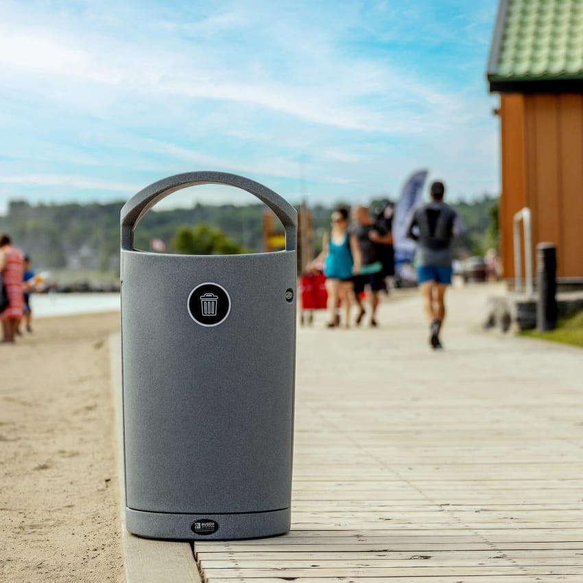 grey trash bin at local beach sitting on boardwalk with people walking by