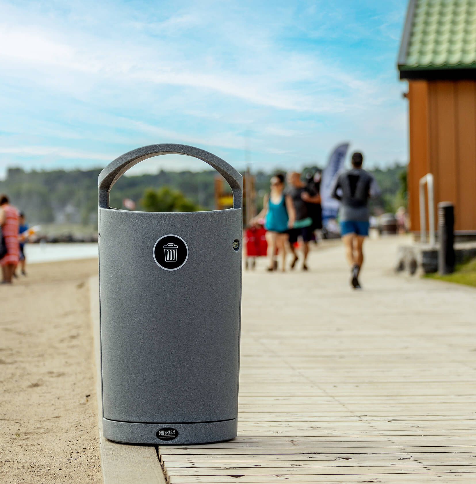 grey trash bin at local beach sitting on boardwalk with people walking by