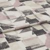 Folded upholstery fabric with distressed geometric triangles and rectangles in muted pink, beige and charcoal — lying layered on a flat surface, close-up under soft studio lighting.
