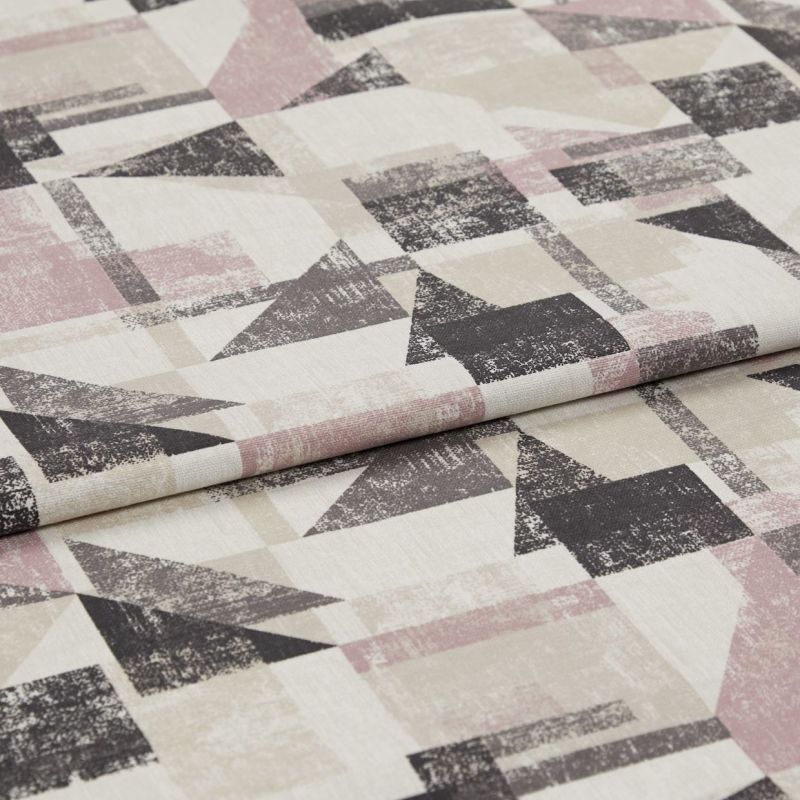 Folded upholstery fabric with distressed geometric triangles and rectangles in muted pink, beige and charcoal â€” lying layered on a flat surface, close-up under soft studio lighting.