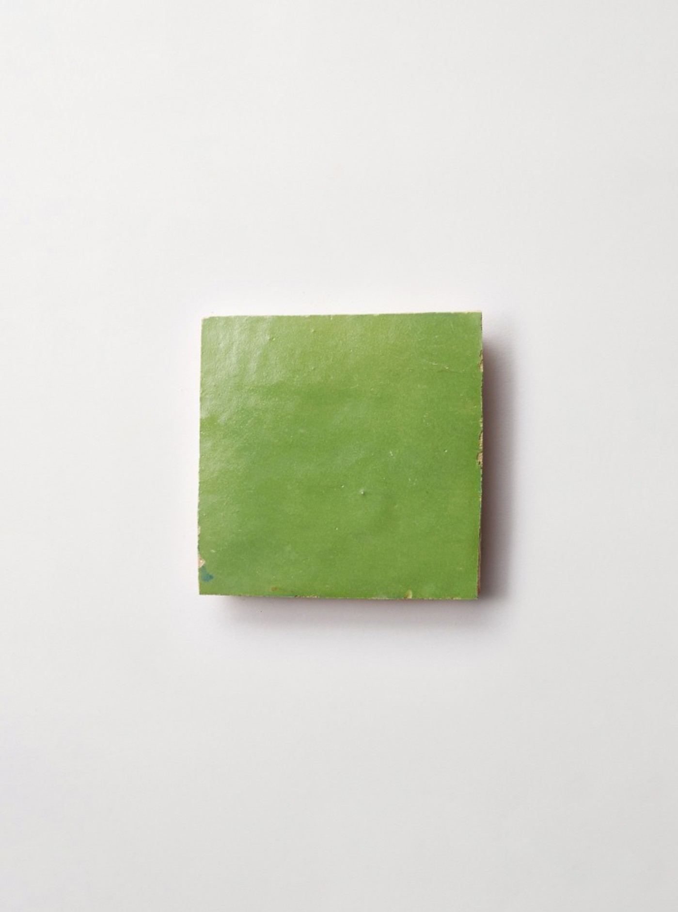 a square piece of green tile on a white surface.