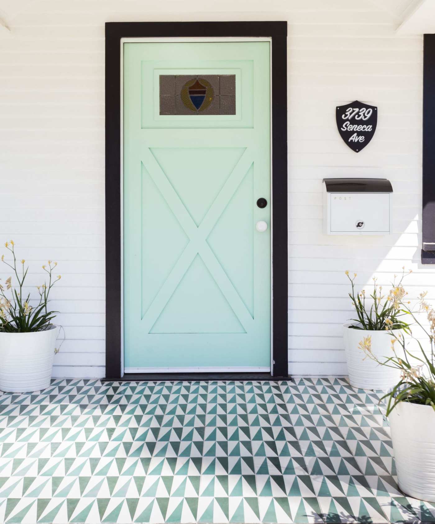 a house with a green door and a tiled porch with potted plants.