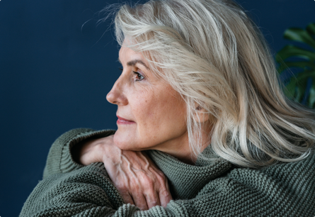 A side view of a woman in a bulky sweater resting her hand on her arms with a thoughtful look on her face.