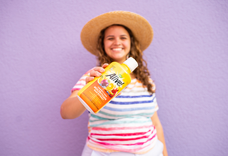 Smiling woman in straw hat holding bottle of Alive Liquid Multivitamin.