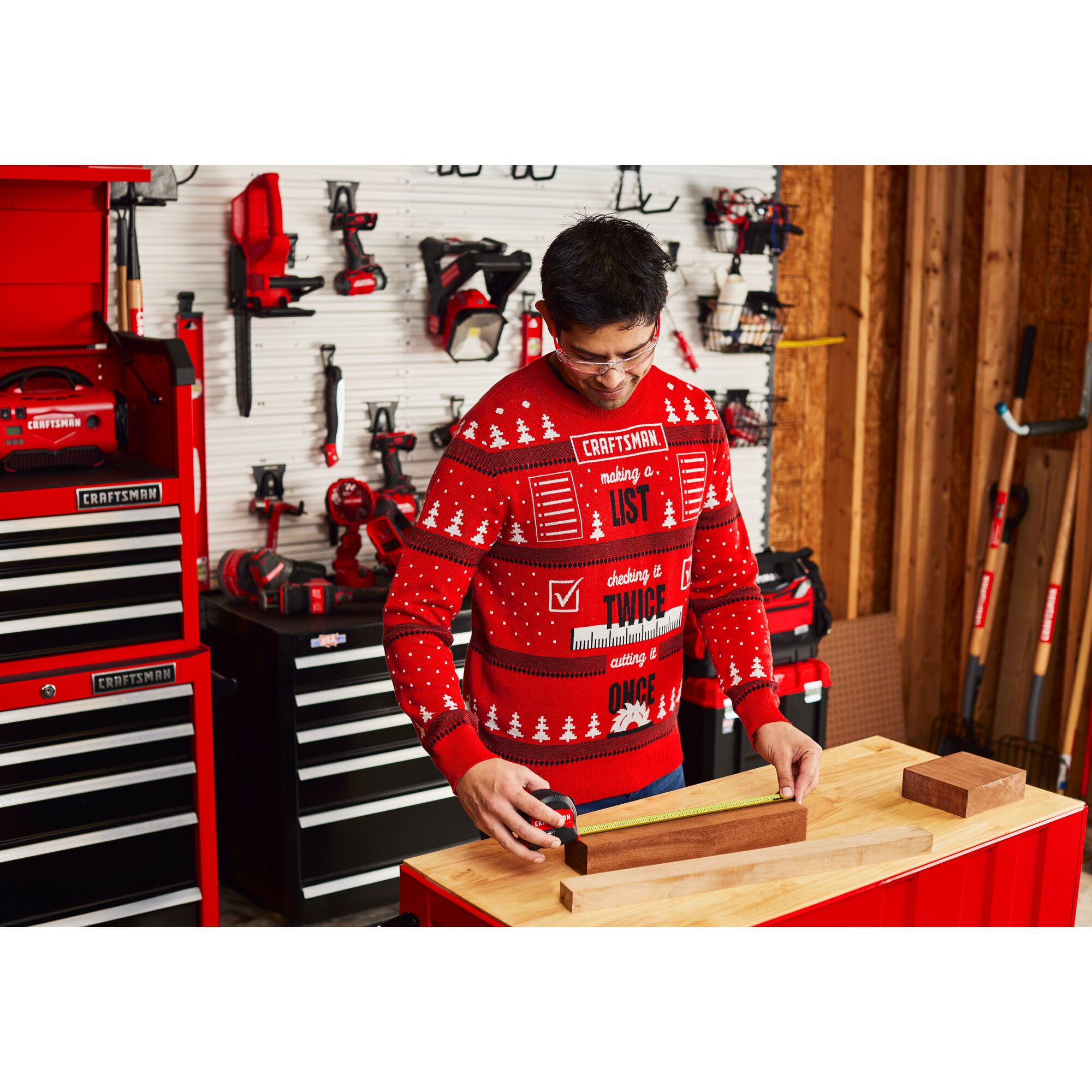 Male in CRAFTSMAN Holiday Sweater measuring wood with measuring tape