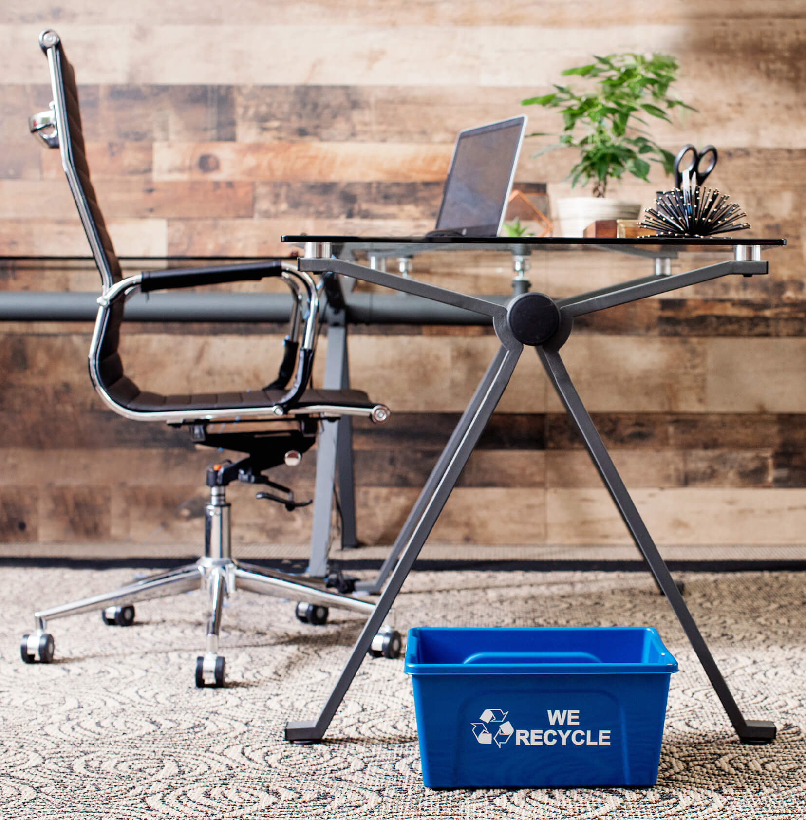 blue deskside recycling bin with we recycle stamped on the side sitting on the floor in a modern office
