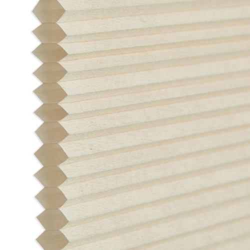 Honeycomb cellular blind, beige pleated fabric with visible hexagonal cell edges at left; closed and flat. Close-up against a neutral white background with soft, diffused indoor lighting.