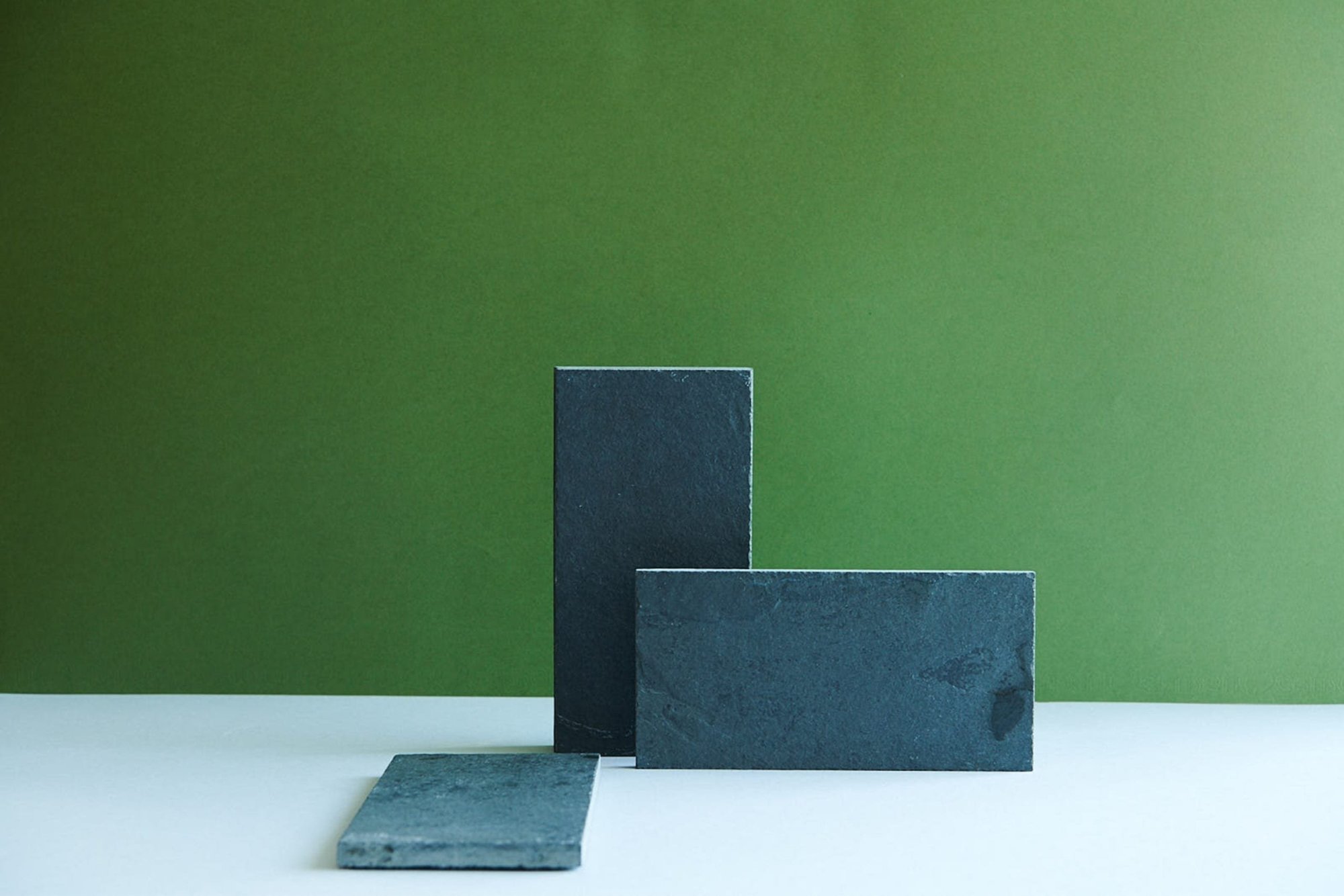 three rectangular black slate tiles on a green background.