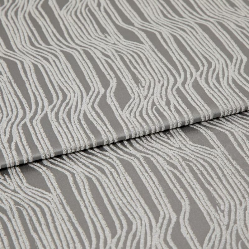 Textured grey upholstery fabric with raised white irregular vertical stripes, folded horizontally across the frame; fabric lies flat in a studio close-up with soft, diffuse lighting highlighting its sheen.