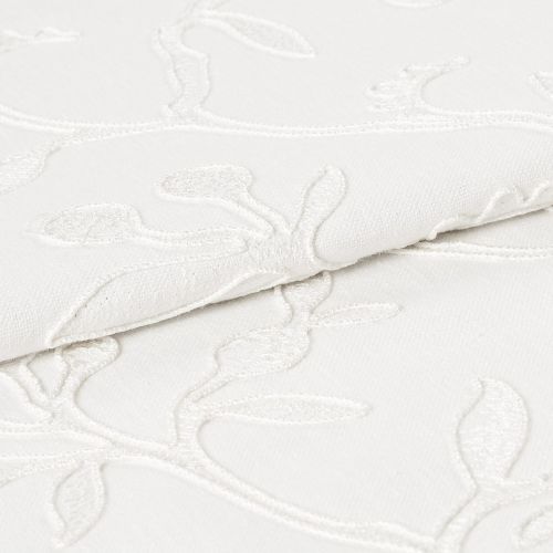 White embroidered fabric folded and overlapping, showing raised floral vine stitching and textured weave; close-up studio view with soft, even lighting emphasizing subtle shadows and fabric detail.