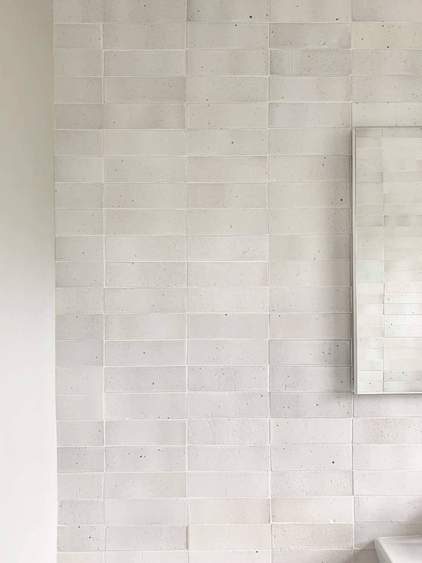 a white tiled bathroom with a sink and mirror.