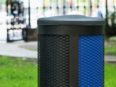 closeup of a triple stream waste and recycling collection bin with a black metal body and black plastic lid in a city park area