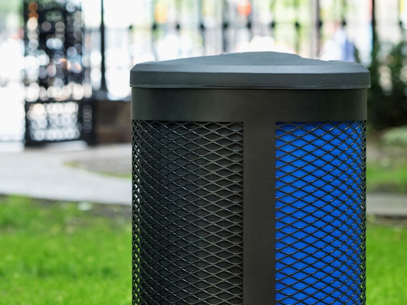 closeup of a triple stream waste and recycling collection bin with a black metal body and black plastic lid in a city park area