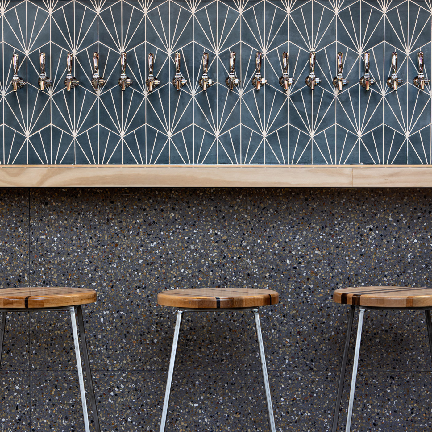 a bar with stools in front of a tiled wall.