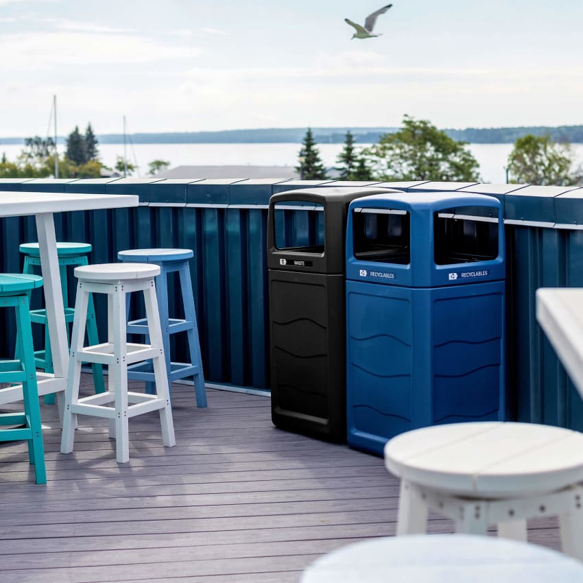 waste and recycling bins in blue and black on a roof top patio with a seagull flying above