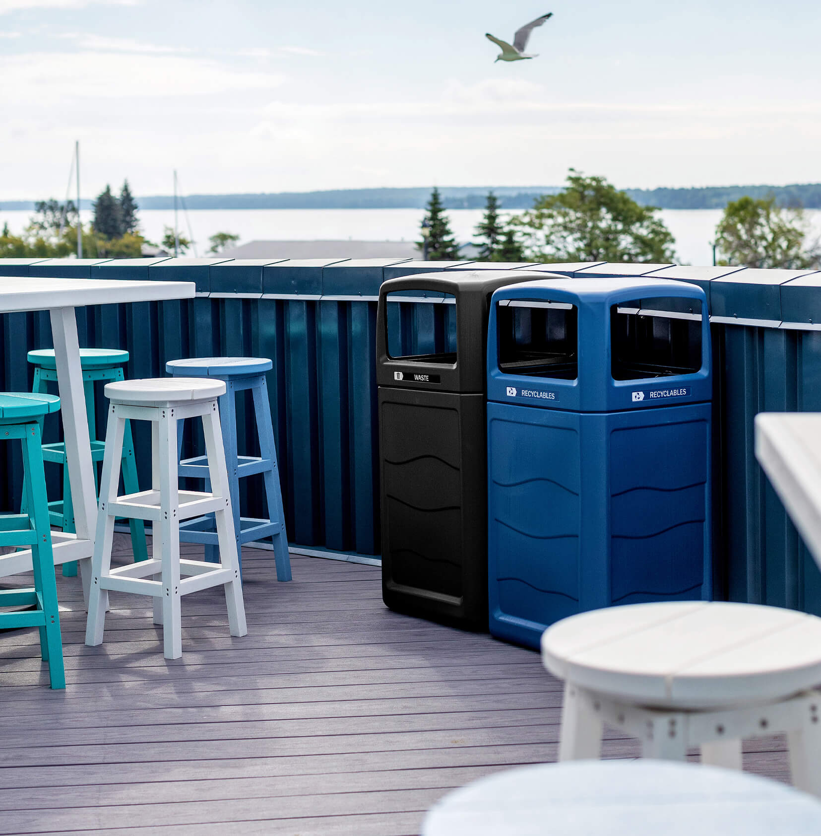 waste and recycling bins in blue and black on a roof top patio with a seagull flying above