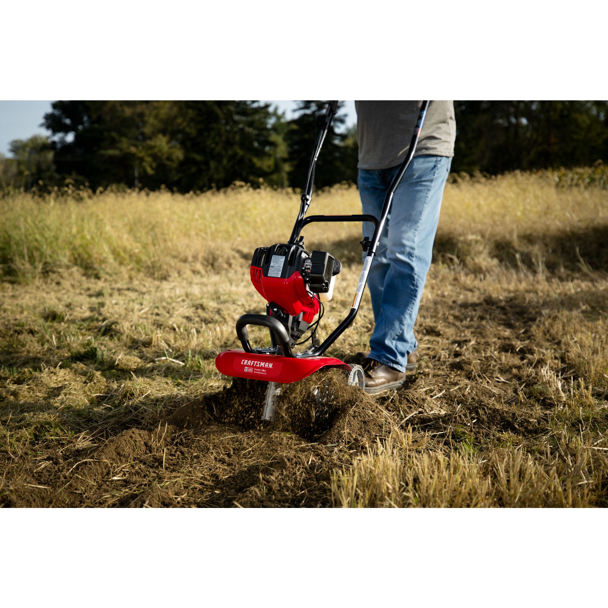 CRAFTSMAN gas cultivator cultivating field in side view in jeans and gray shirt