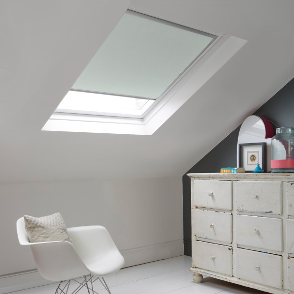 Room with white eaves wall, dark blue-grey wall to right with a shabby chic white drawer unit, a contemporary white chair, white painted floorboards and a skylight blind in pale grey.