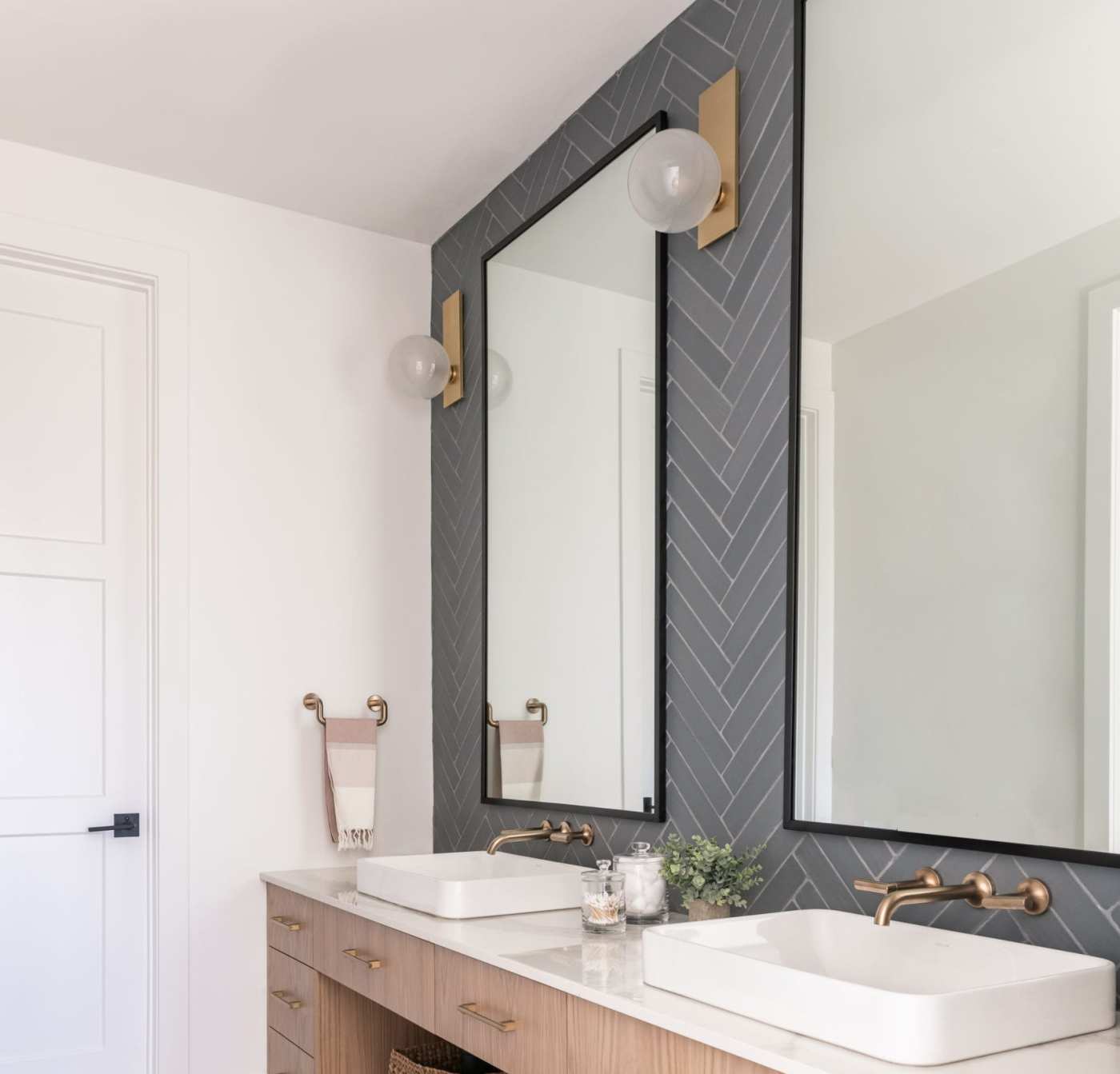 a bathroom with two sinks and a two mirror in front of a grey tiled wall.