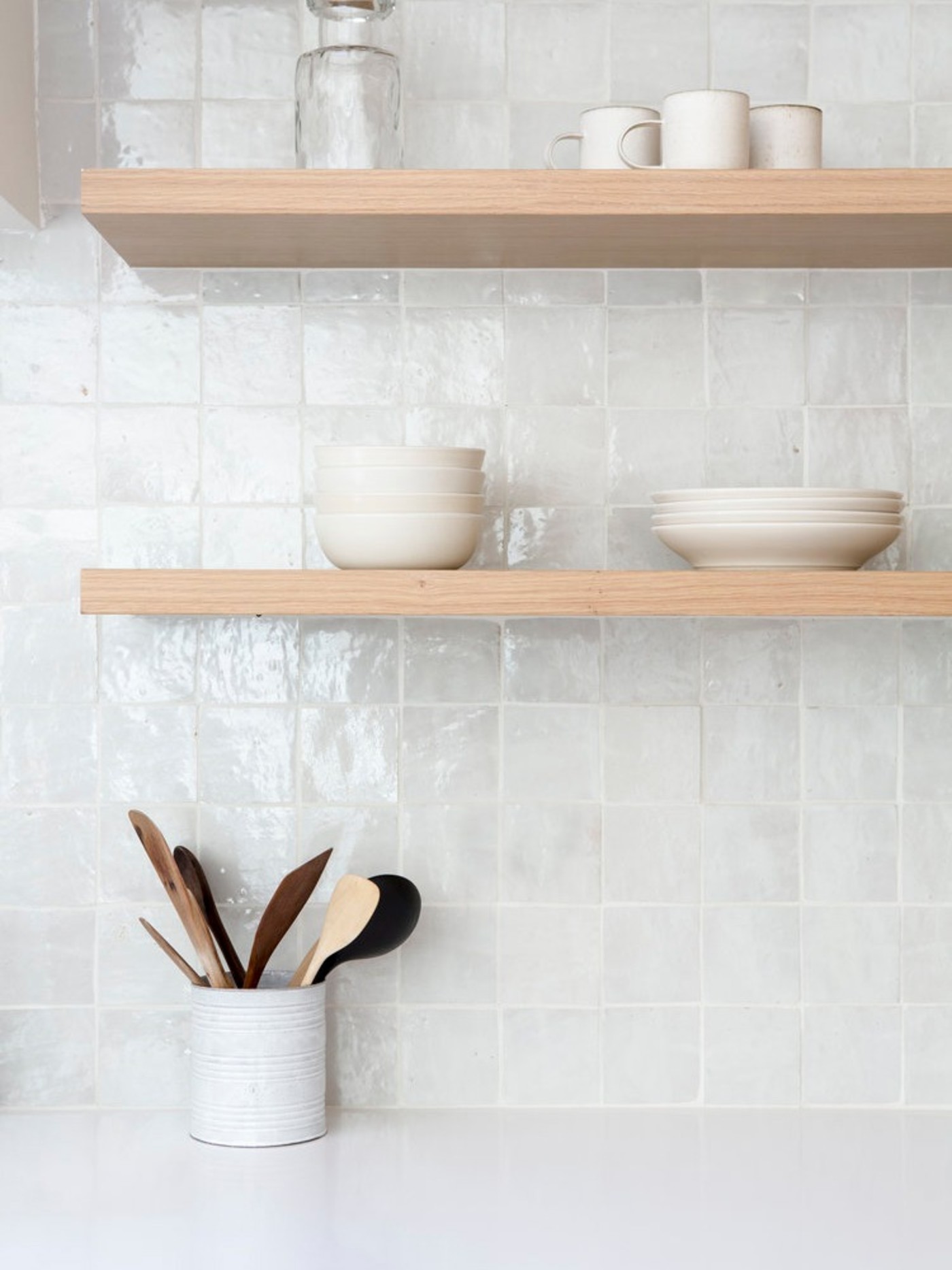 a white tle kitchen backsplash with wooden shelves and utensils.