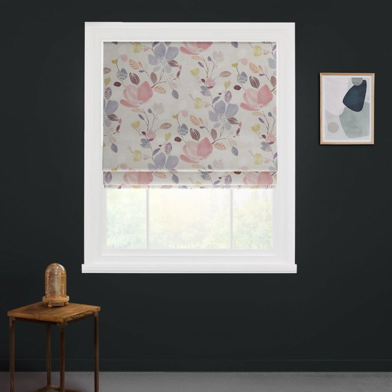 Floral Roman blind, lowered over a white window, softly filtering daylight; in a dark-painted room with a wooden side table bearing a glass cloche lamp and a framed abstract print.