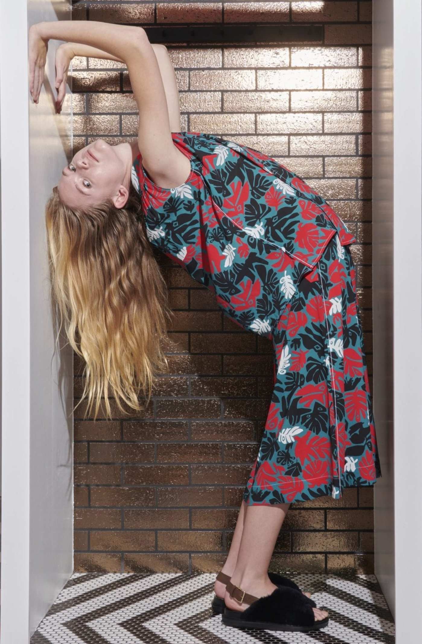 a woman in a floral dress arching her back in a tiled alcove.