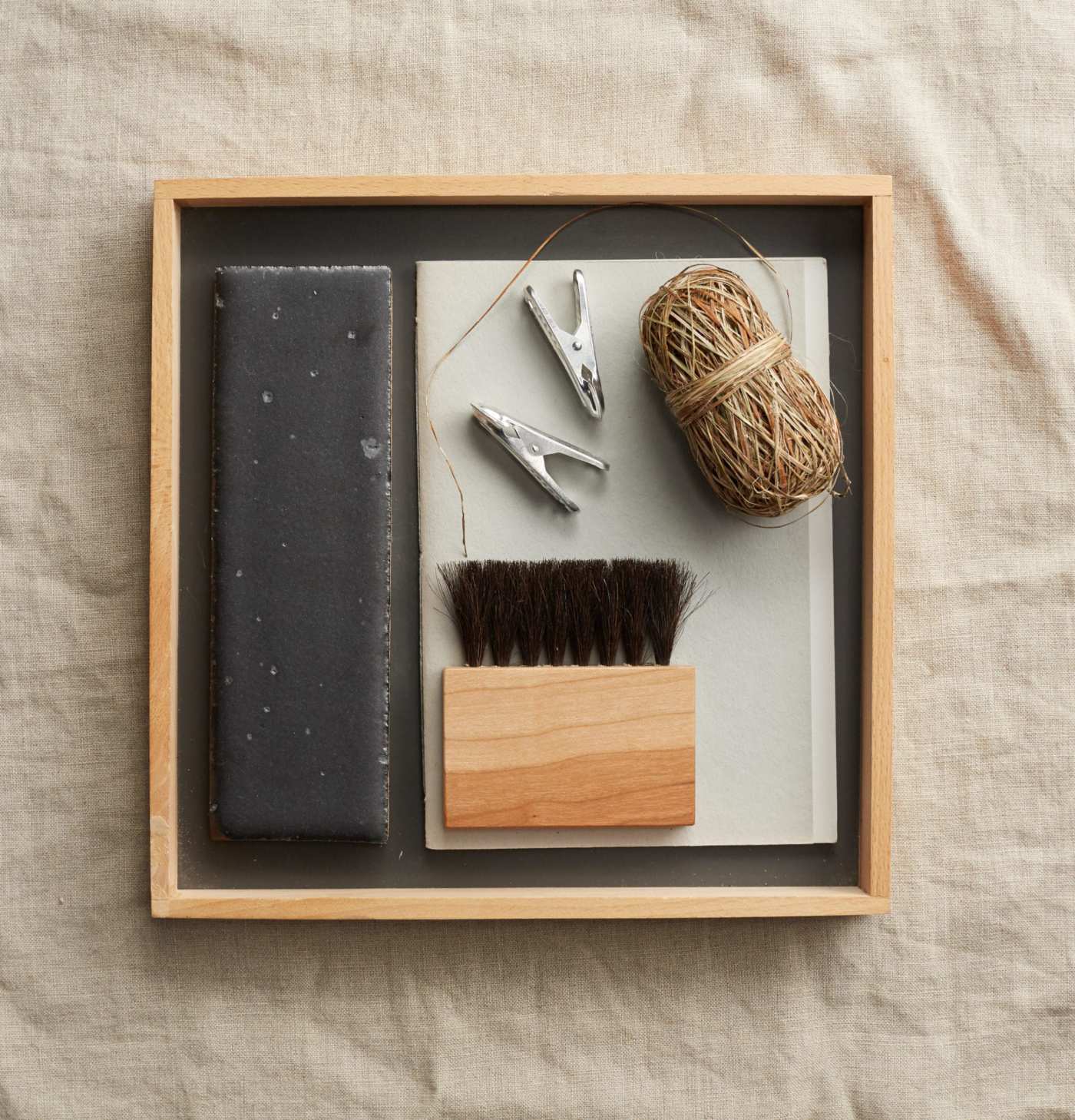 a wooden box containing a black rectangle tile, a brush and yarn.