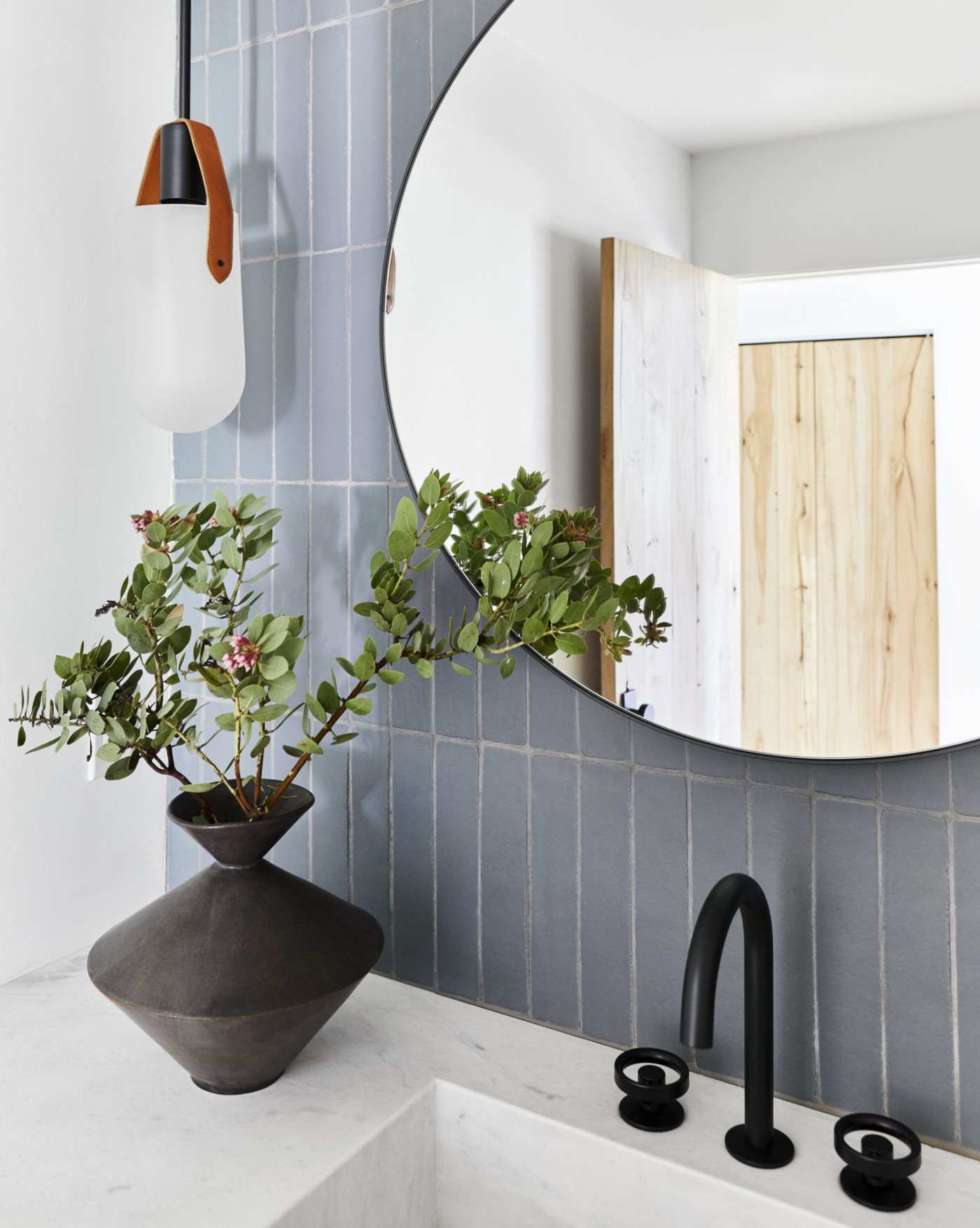 a bathroom with a sink, a blue tiled wall and a round mirror.