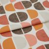 Printed fabric featuring repeated halfâ€‘circle motifs in orange, rust, beige and textured brown, folded once across the frame, photographed close-up on a neutral surface with soft, even lighting.