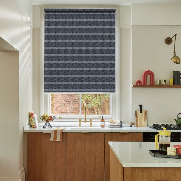 Navy horizontally striped roller blind lowered across the sash, filtering light and covering most of the window; kitchen with brass faucet, marble counters, wooden cabinets and a brick courtyard outside.