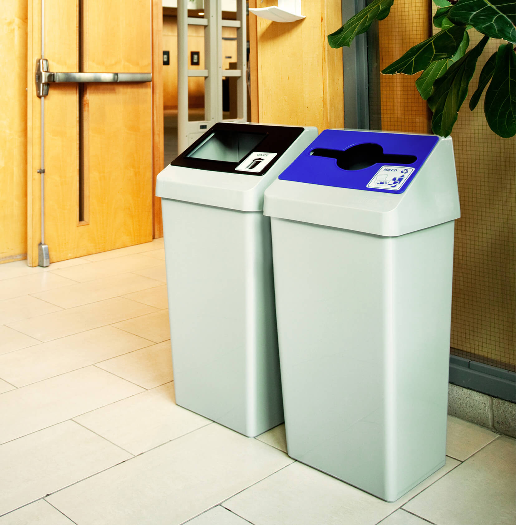 double waste and recycling station with grey body and colored restrictive opening lids in a college hallway