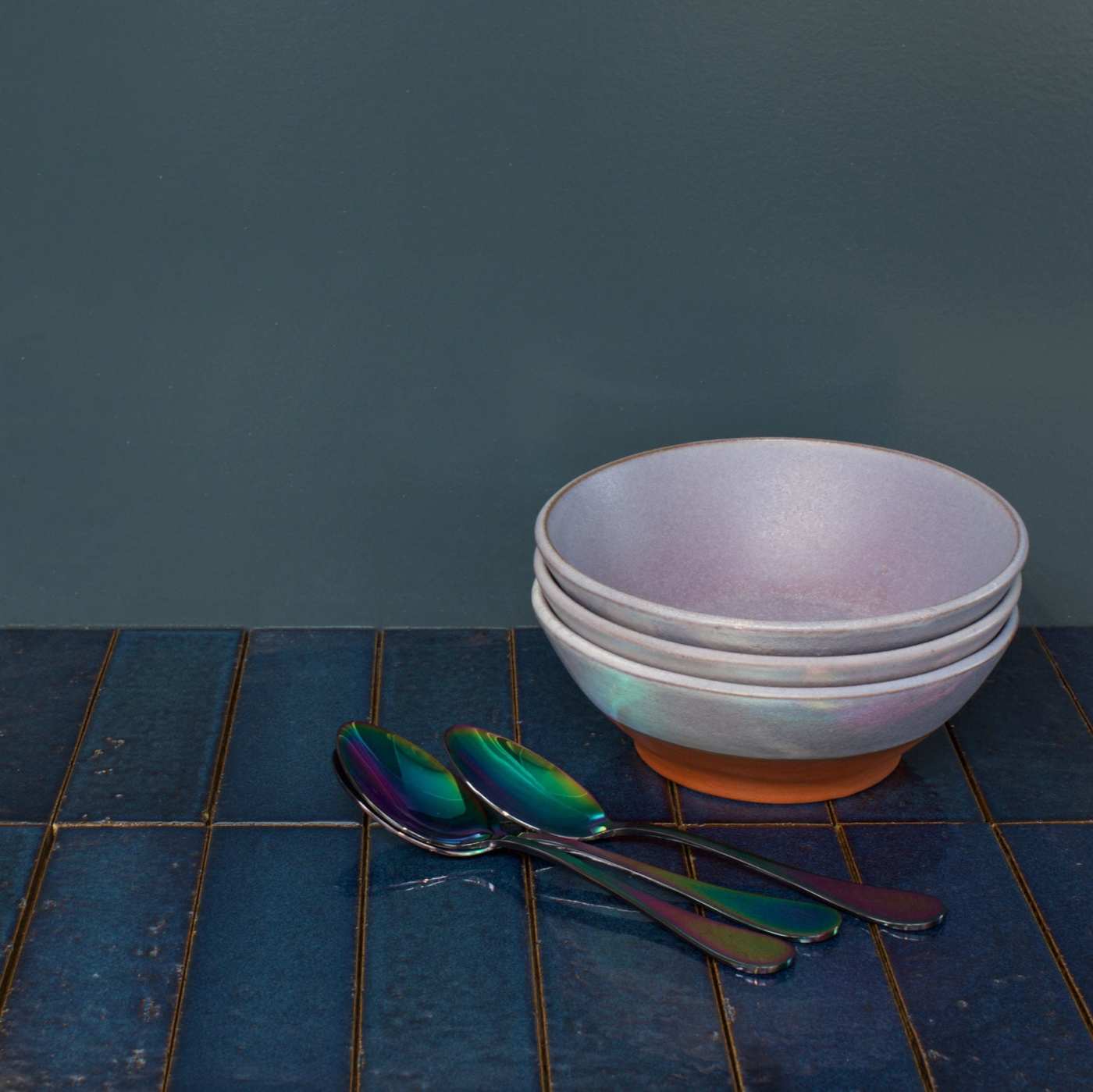 a bowl and two spoons on a blue tiled counter.